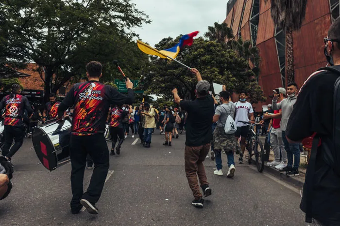 Percusionistas y manifestantes con banderas de Colombia caminan por una calle durante la marcha