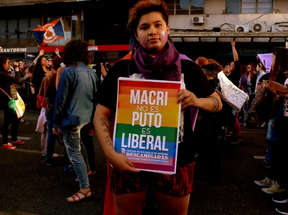 Persona en una marcha sosteniendo un cartel con los colores arcoíris «Macri no es puto es liberal»