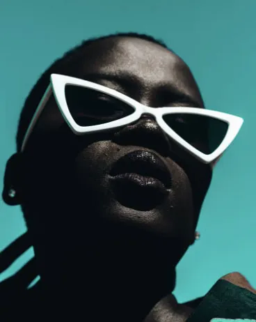 Persona con gafas blancas de ojo de gato sobre fondo turquesa, vista desde abajo