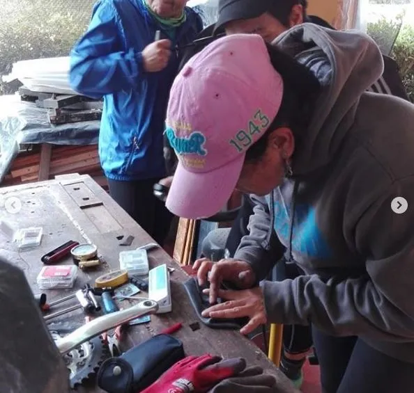 Persona con gorra rosa y sudadera repara un aparato sobre una mesa con herramientas
