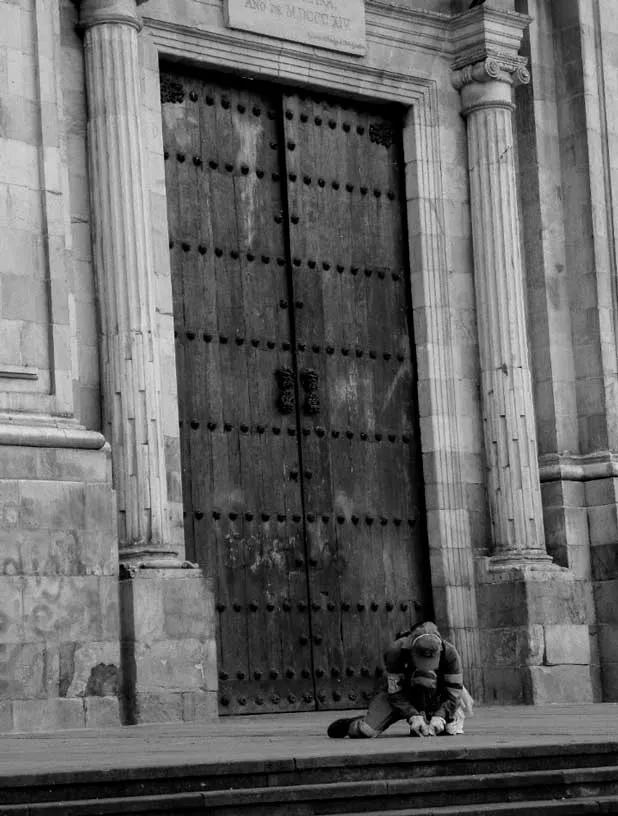 Persona sentada sola ante el portón de madera de una iglesia del centro de Bogotá, en blanco y negro