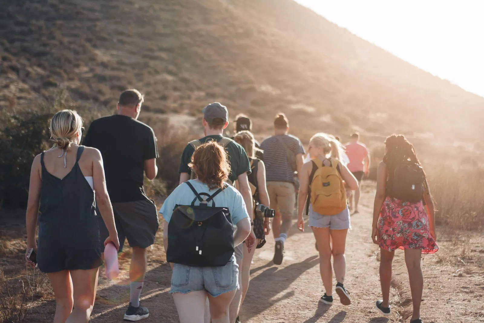 Grupo de personas caminando de espaldas por un sendero de montaña al atardecer