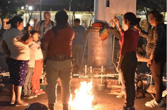 Personas reunidas de noche junto a una fogata frente a un memorial de cruces en Guatemala