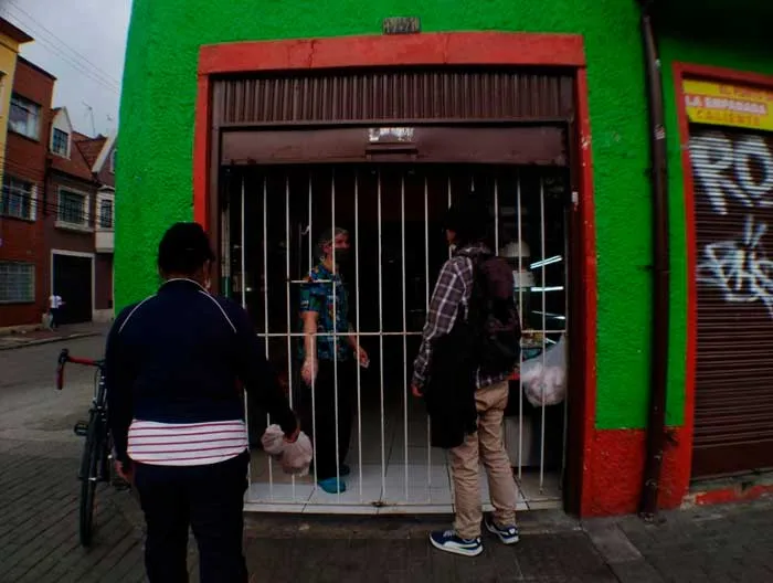 Personas frente a un local de fachada verde y roja con reja metálica en una calle de Bogotá durante la cuarentena