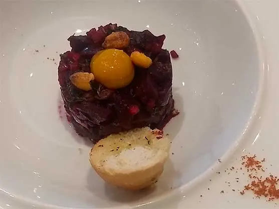 Plato de tártaro de remolacha con yema y frutos secos y un pan pequeño