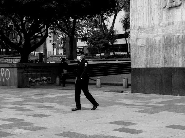 Policía camina por una plaza casi vacía del centro de Bogotá durante la cuarentena, en blanco y negro