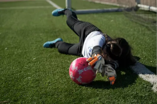 Portera de fútbol tendida en el césped atrapa un balón rosado frente al arco