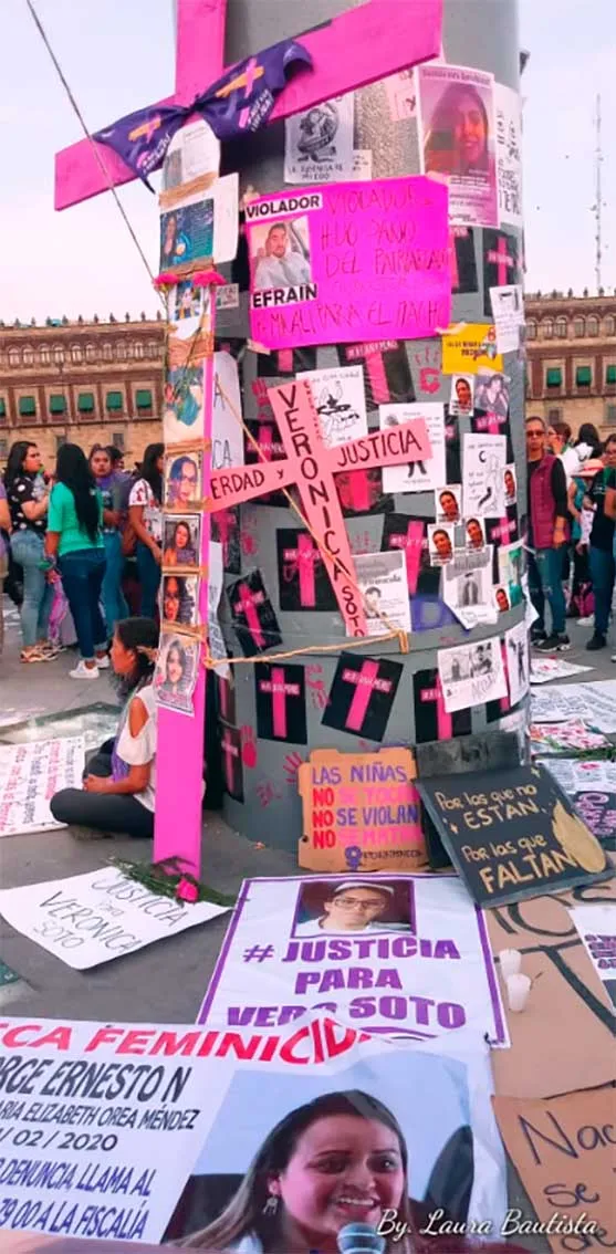Poste cubierto de cruces rosadas, fotos y carteles de «Justicia» en un memorial feminista en la plaza