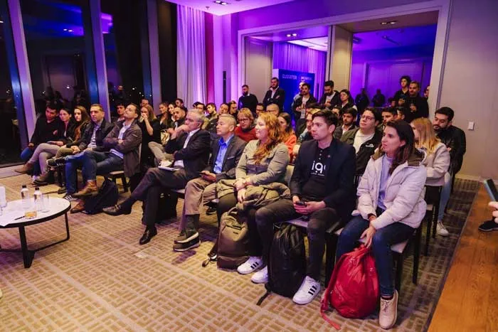 Público sentado en un salón con luz morada escuchando una charla del evento de Clouxter