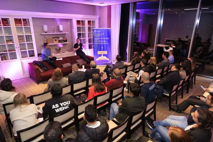 Público sentado en un salón de un evento de Clouxter mientras dos personas hablan al fondo