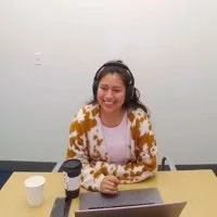 Rebeca López Valerio, con audífonos y sonrisa, sentada ante una mesa con un portátil y una taza