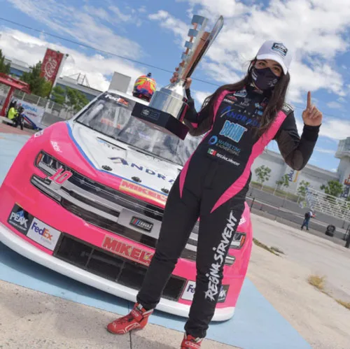 Regina Sirvent, piloto, de pie junto a su auto de carreras rosa con un trofeo