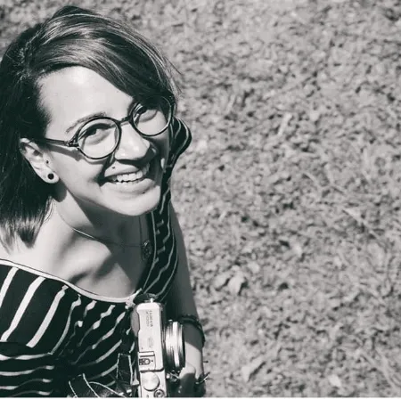 Retrato en blanco y negro de una fotógrafa sonriente con gafas y una cámara colgada al cuello