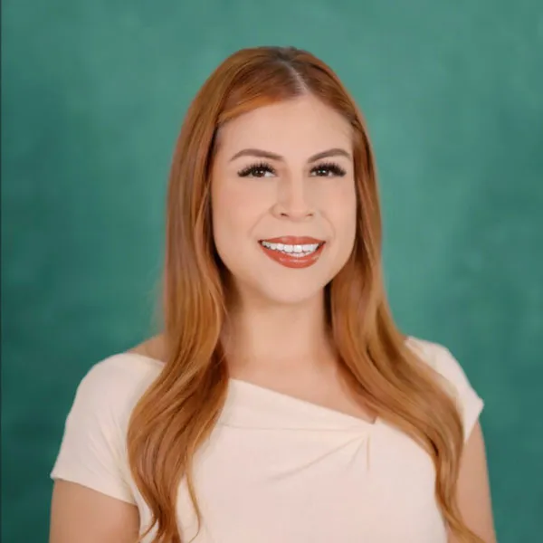 Retrato de Marisol Espinoza, sonriente, de cabello largo castaño rojizo, sobre fondo verde azulado