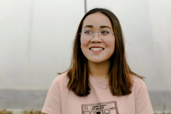 Retrato de una mujer joven sonriente con gafas, cabello castaño y camiseta rosa