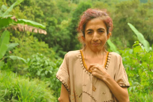 Retrato de Nazareth, mujer de cabello rojizo con blusa beige, entre la vegetación