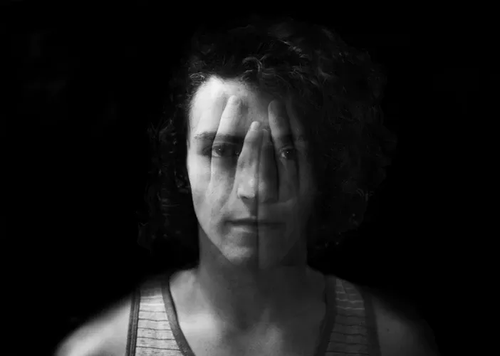 Retrato en blanco y negro de una persona de cabello rizado que se cubre un ojo con la mano