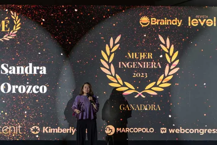 Mujer en el escenario con micrófono ante una pantalla que muestra «Sandra Orozco» y «Mujer Ingeniera 2023, Ganadora»