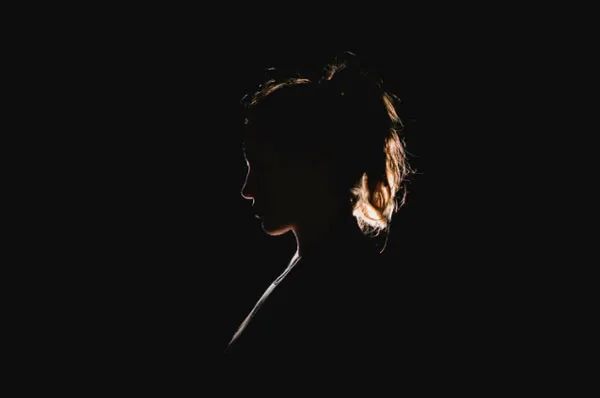 Silueta de perfil de una mujer en la oscuridad con luz sobre el cabello