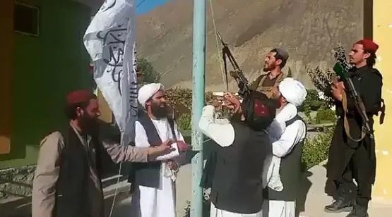 Hombres armados y de turbante junto a un mástil izan una bandera blanca del régimen talibán en Afganistán