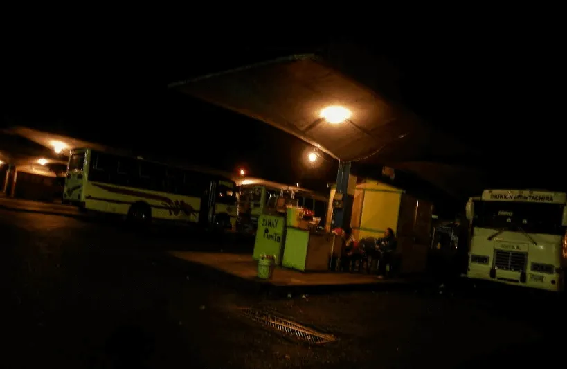 Terminal de buses casi a oscuras de noche con autobuses estacionados y una luz encendida