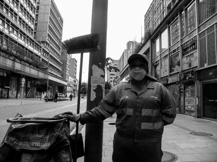 Trabajador de aseo con chaleco reflectivo y tapabocas junto a un poste en una calle de Bogotá