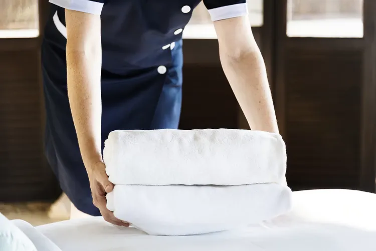 Trabajadora con uniforme azul acomoda toallas blancas dobladas sobre una cama