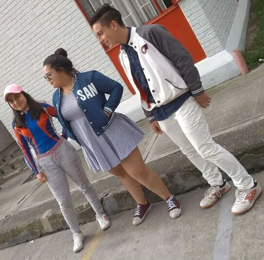 Tres jóvenes de pie sobre una acera, dos mujeres y un hombre con chaquetas