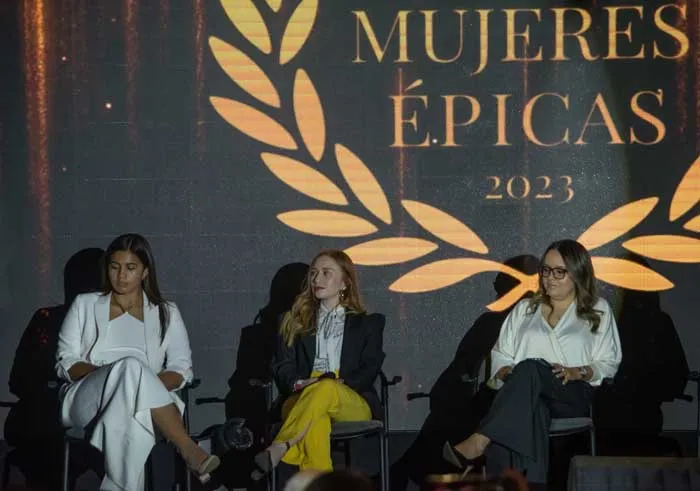 Tres mujeres sentadas en un panel bajo el logo «Mujeres Épicas 2023»