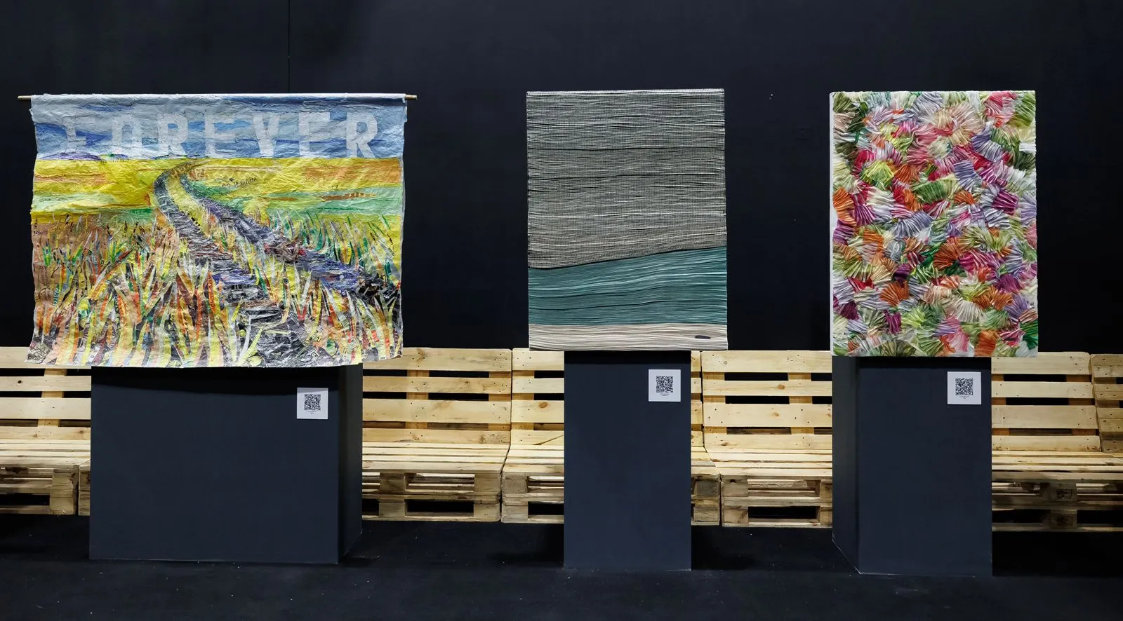 Tres obras textiles colgadas en una muestra de arte, una con la palabra «Forever»
