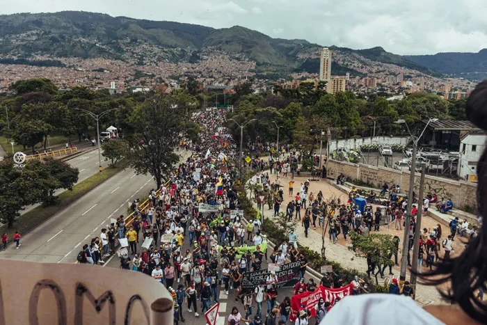 Vista elevada de una multitud que marcha por una avenida con montañas y ciudad al fondo