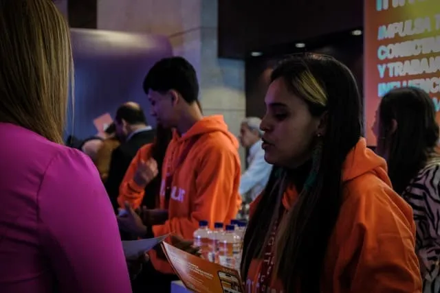 Asistentes con sudaderas naranjas de pie en el pasillo del WebCongress Multiverse